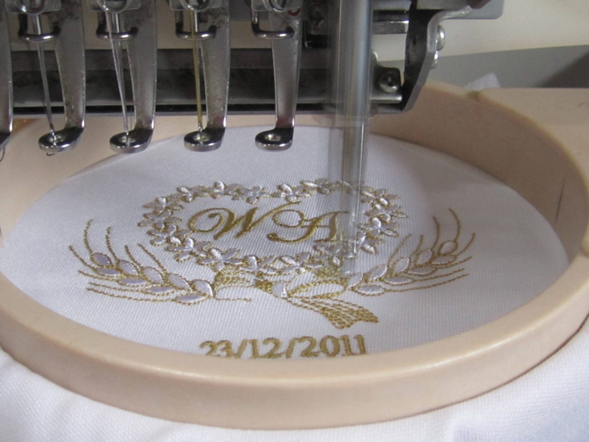 Goldenes Monogramm mit Blumenkranz, frisch gestickt, noch im Rahmen unter der Nadel