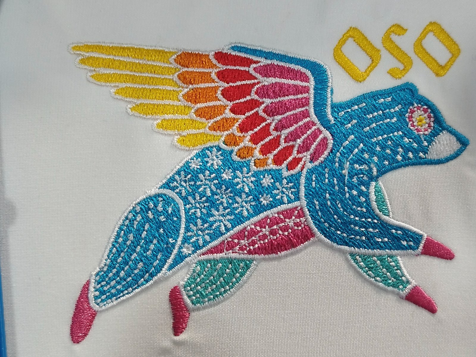Multicolor alebrije bear sew-out with gradient wings and decorative run stitch on white fabric